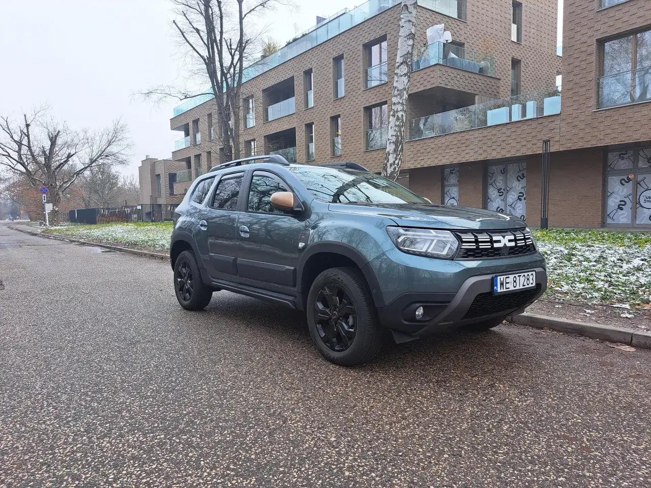 Zielony Dacia Duster na tle nowoczesnego budynku. Zastanawiasz się nad dacia duster spalanie? Ten model oferuje rozsądne zużycie paliwa.