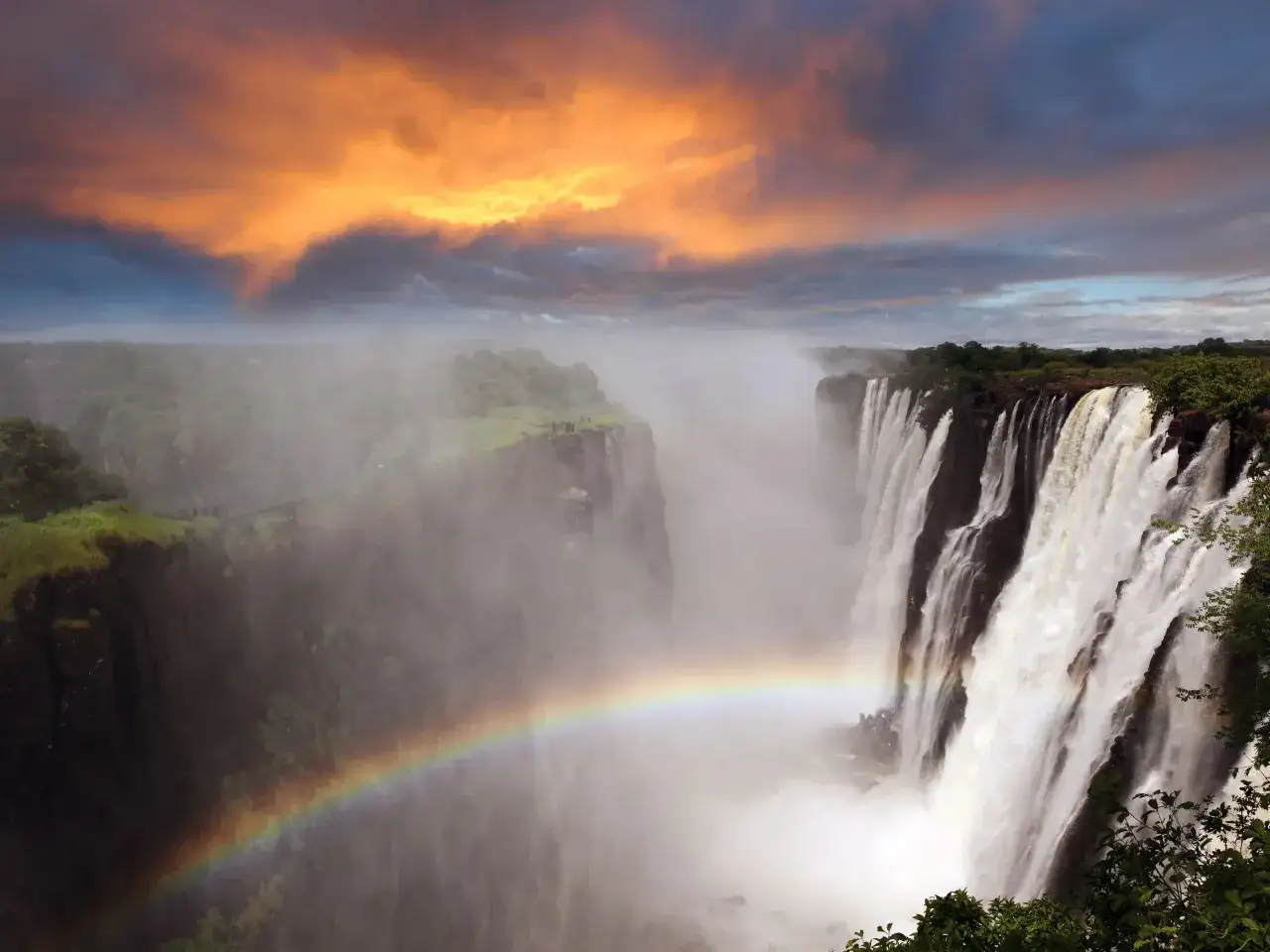 Spektakularne wodospady Wiktorii w Zimbabwe, z tęczą i burzowymi chmurami. Niezapomniane atrakcje Afryki.