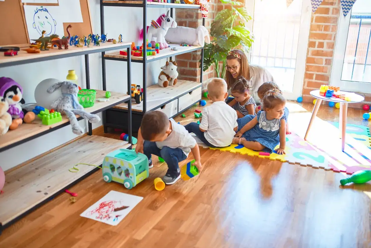 Wesoła opiekunka bawi się z kilkorgiem dzieci. Widać, ile dzieci przypada na jednego opiekuna w przedszkolu.