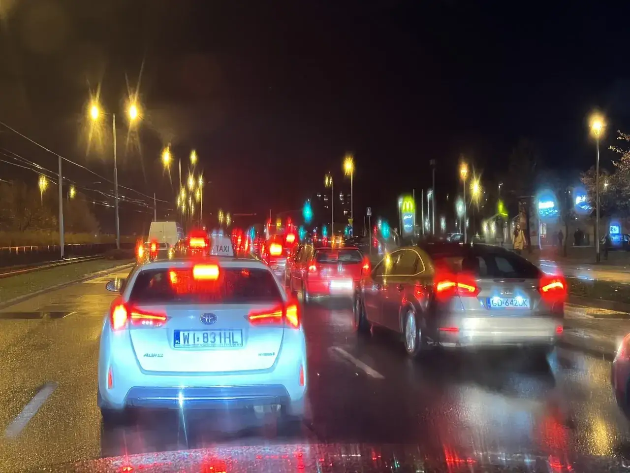 Nocne natężenie ruchu w Gdyni. Samochody stoją w korku, widać światła uliczne i znaki drogowe.