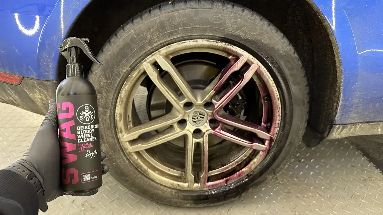 Rękawica w czarnej rękawiczce trzyma butelkę środka do czyszczenia felg. Pokazuje, jak umyć felgi, aplikując fioletowy płyn na brudną felgę Porsche.