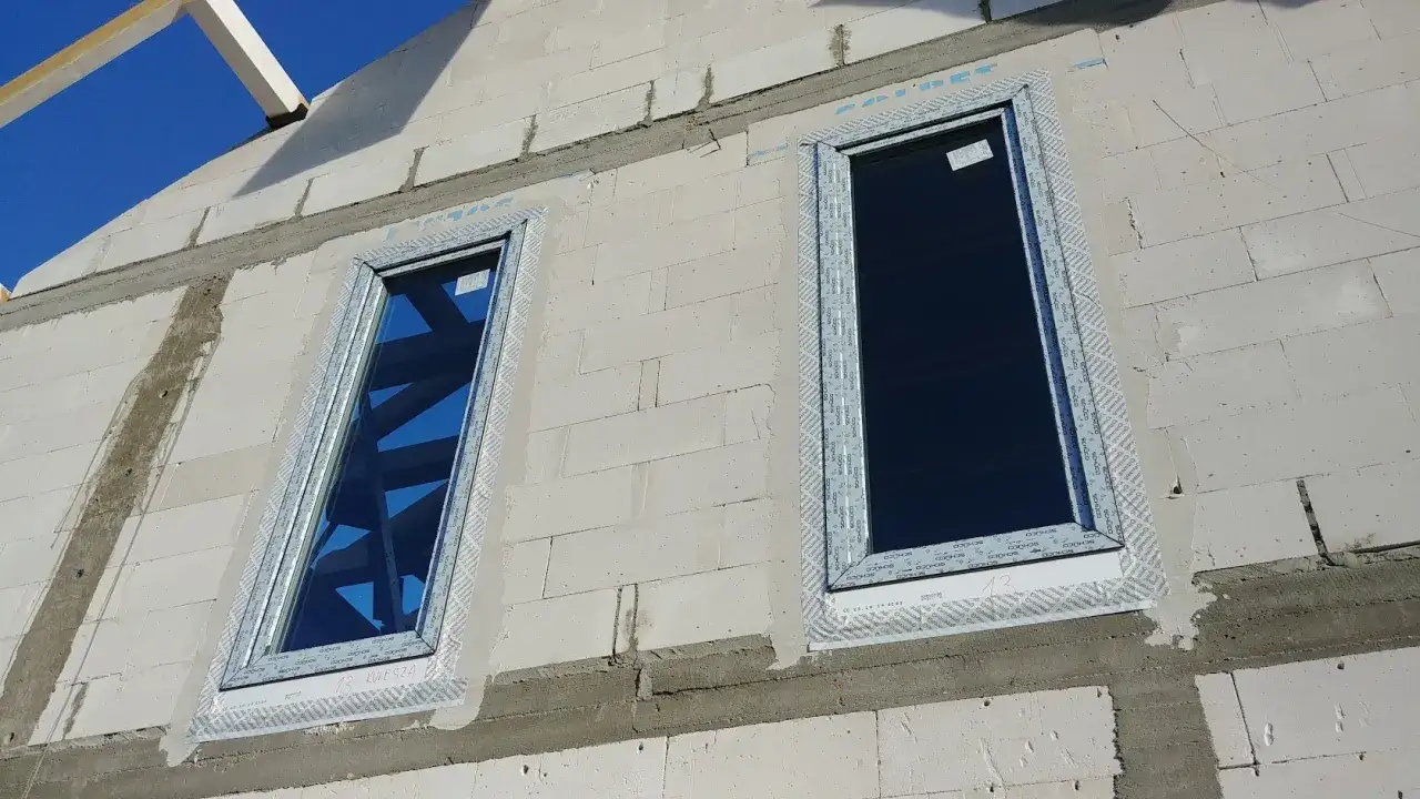 Montaż okien: pianka izolacyjna wokół ram okiennych, widoczne bloczki z betonu komórkowego i fragment dachu.