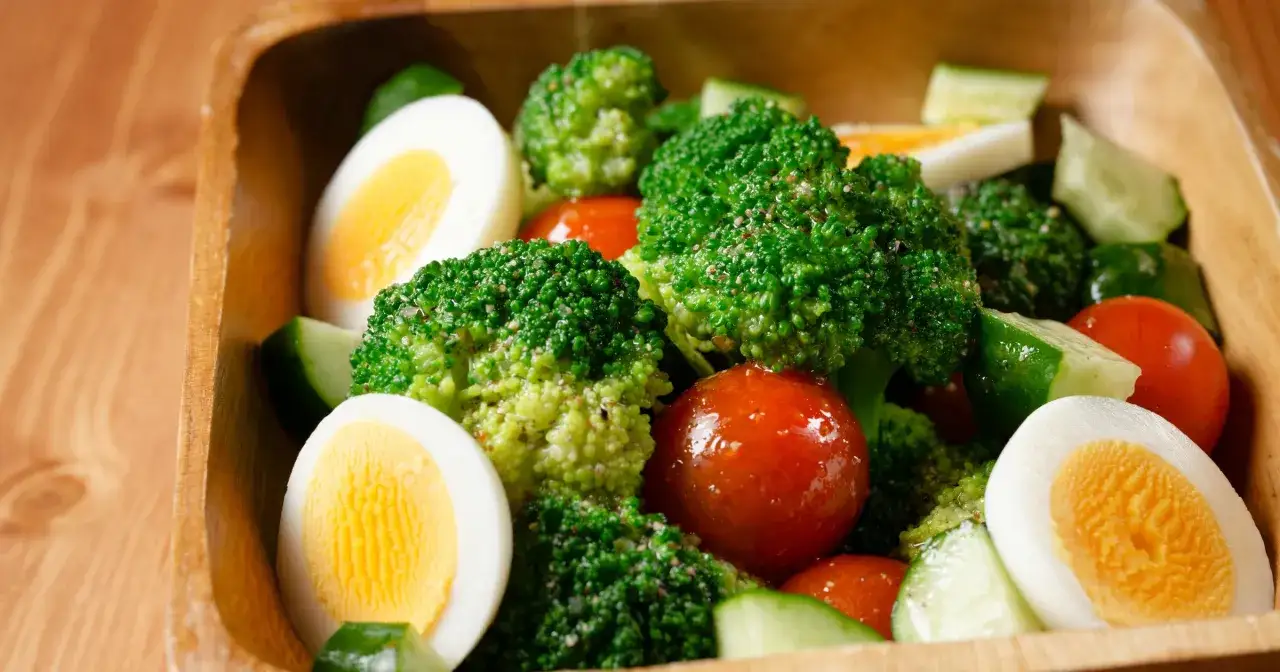 Sałatka z brokułem, jajkiem, pomidorem i ogórkiem, posypana pieprzem. Wygląda apetycznie!