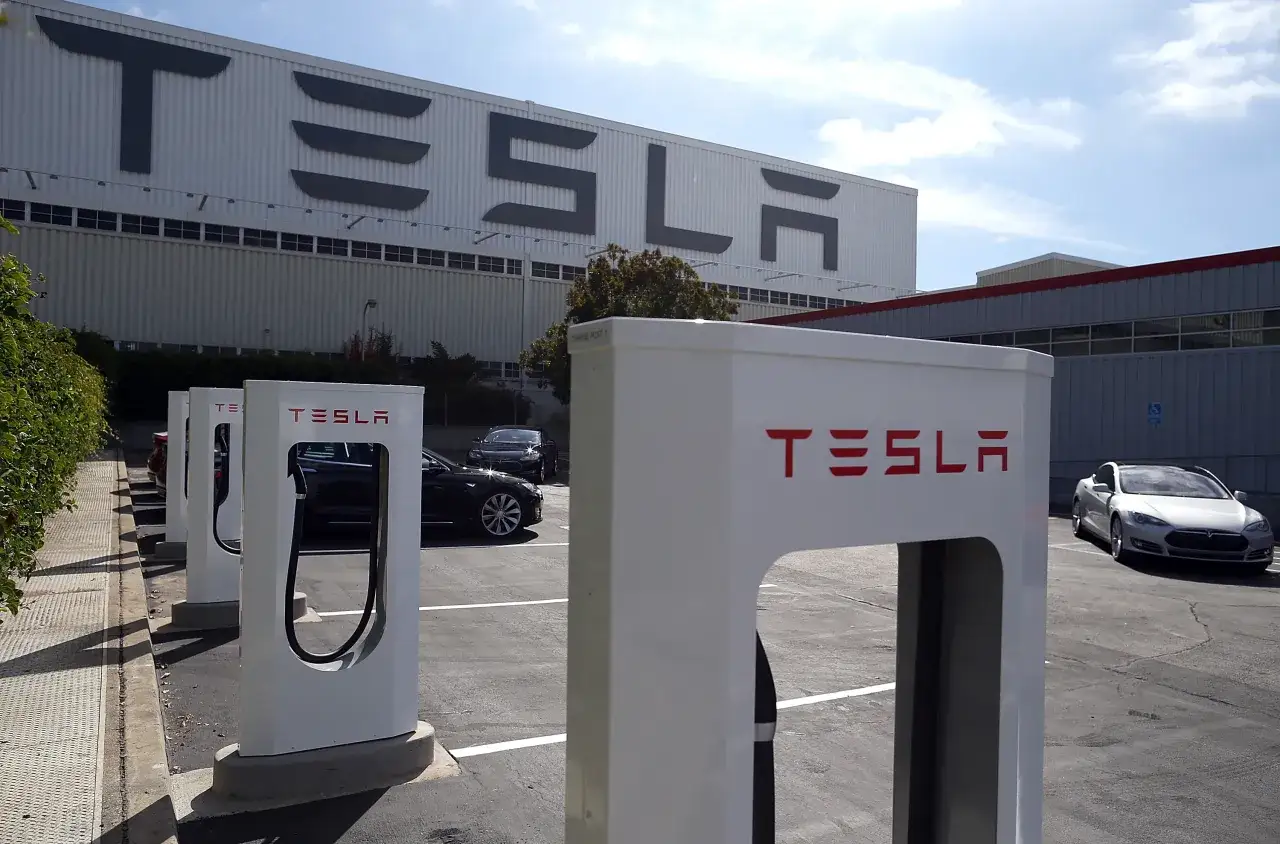 Ładowarki Tesli przed budynkiem z logo firmy. Tesla to marka z USA, znana z innowacyjnych samochodów elektrycznych.