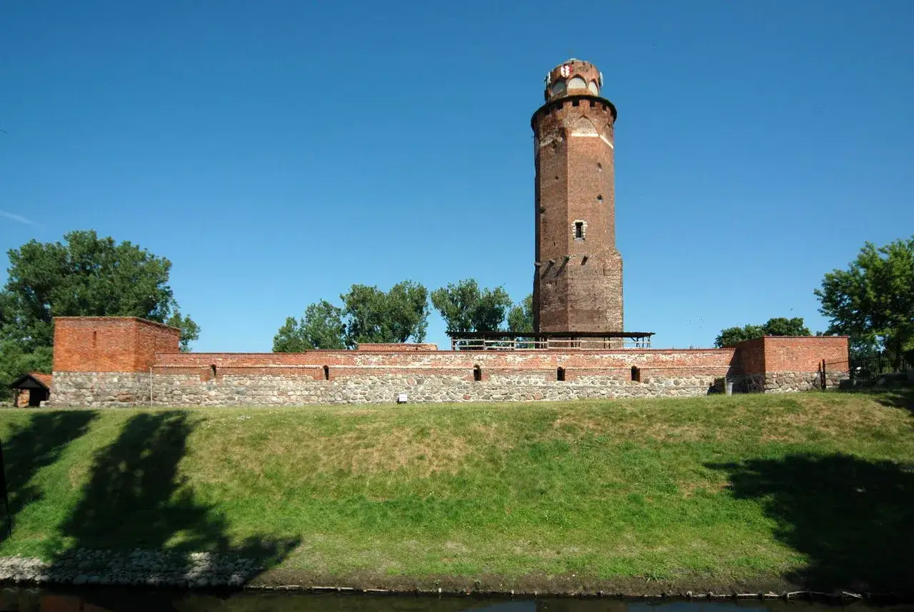Zamek krzyżacki w Brodnicy, potężna wieża i mury obronne na tle błękitnego nieba.