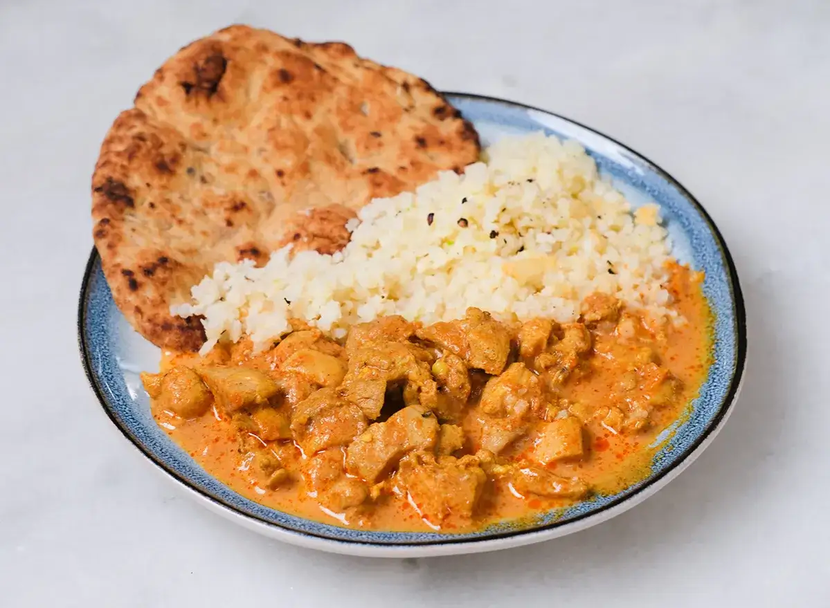 Pyszny kurczak tikka masala z ryżem i plackiem naan na talerzu.