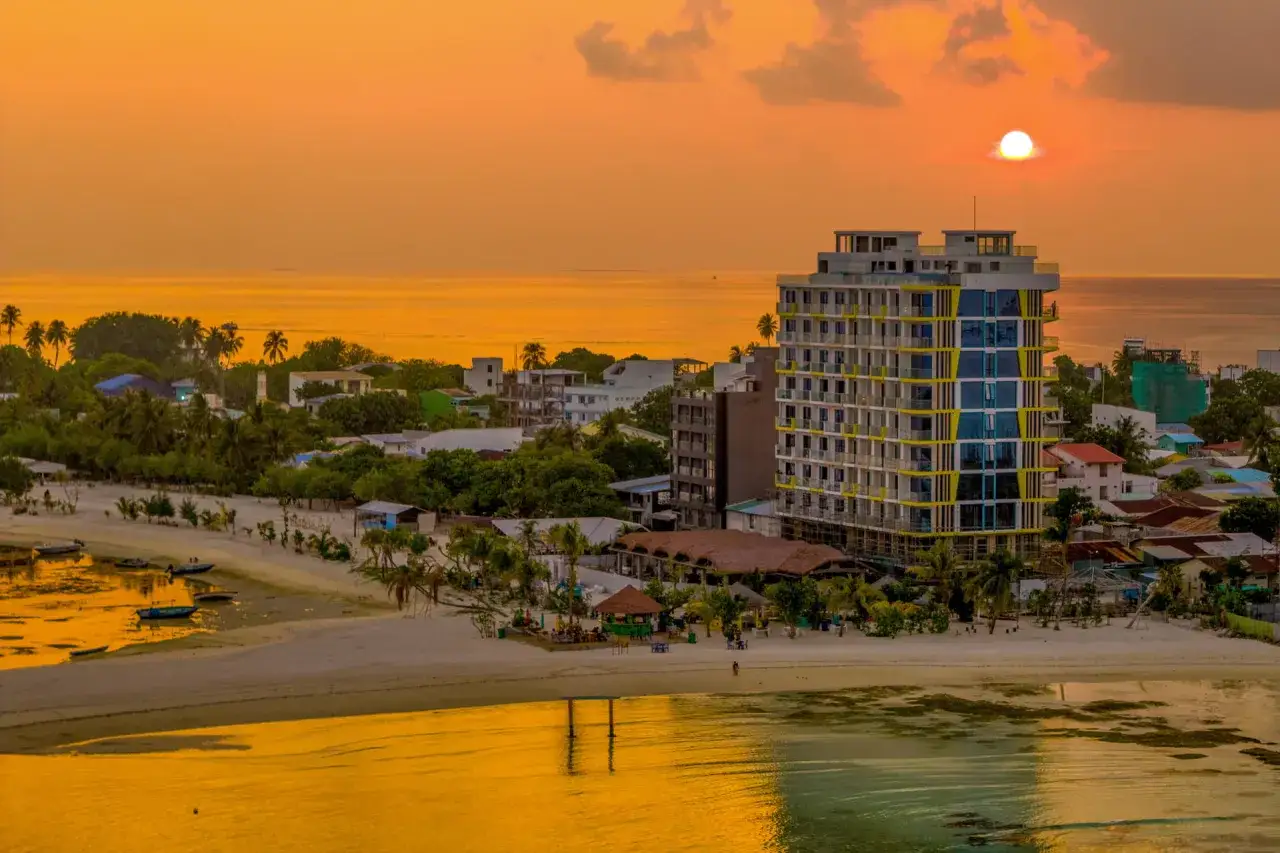 Zachód słońca na Malediwach. Piękna plaża, palmy i nowoczesny hotel. Kiedy najlepiej jechać na Malediwy? W porze suchej, od listopada do kwietnia.