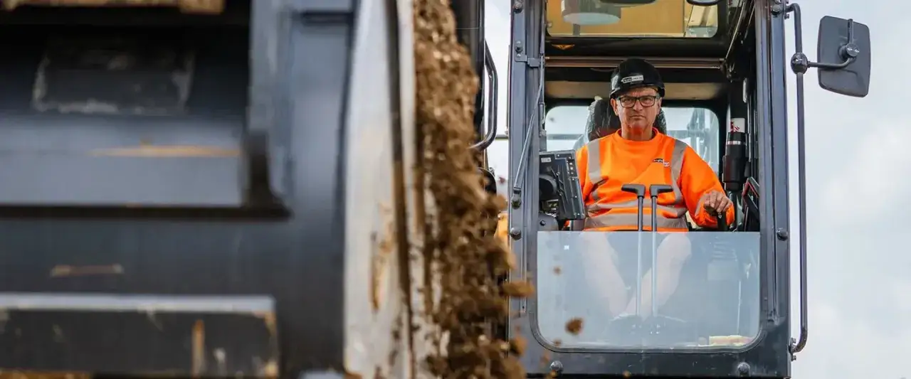 Operator koparki w kamizelce odblaskowej, zastanawia się, ile zarabia operator koparki na godzinę.