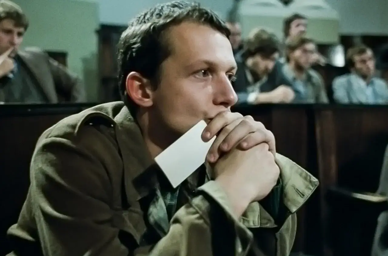 Młody mężczyzna z kartką w dłoniach, zamyślony, w sali sądowej. Scena z kina moralnego niepokoju.