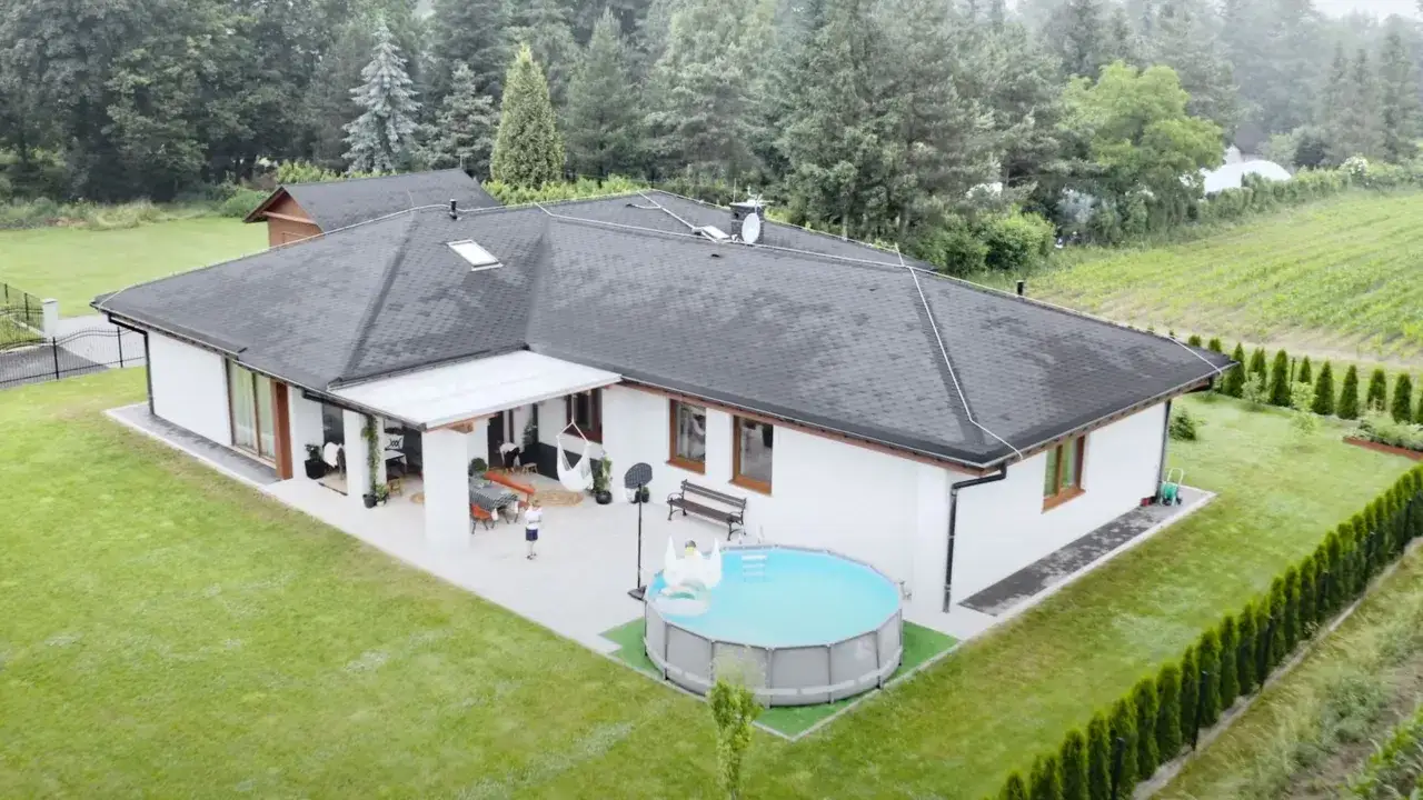 Nowoczesny dom z perlitu otoczony zielenią, z basenem i placem zabaw.