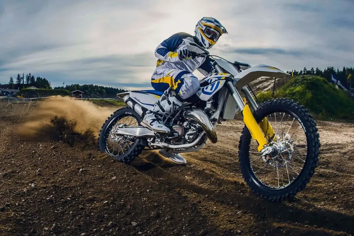 Motocyklista na motocyklu Husqvarna śmiga po torze, wzbijając tumany kurzu.