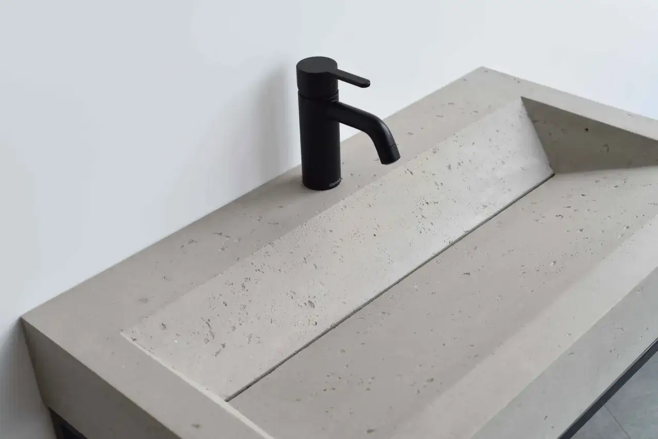 Nowoczesna umywalka z betonu o geometrycznym kształcie, z czarną, minimalistyczną baterią.