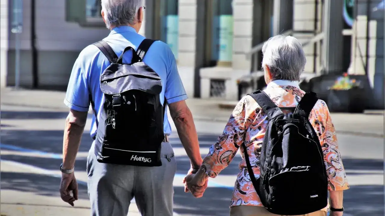 Seniorzy z plecakami, trzymając się za ręce, spacerują. Czy doczekają się wsparcia w postaci bonu turystycznego dla senior&oacute;w?