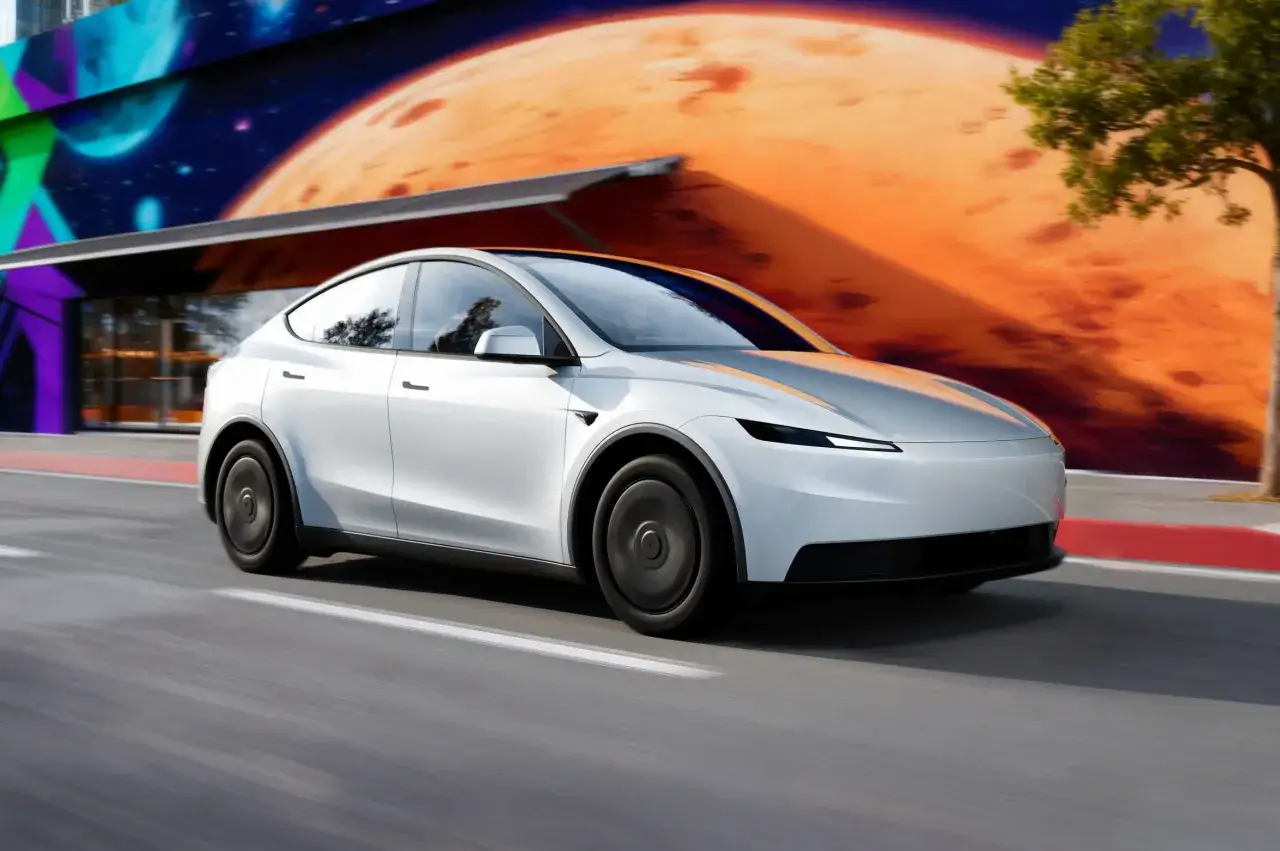 Biały Tesla Y pędzi ulicą. Czy warto kupić ten elektryczny SUV? Tło z kosmicznym muralem dodaje futurystycznego klimatu.