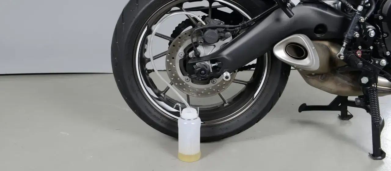 Wymiana płynu hamulcowego w motocyklu: przezroczysty wężyk podłączony do zacisku hamulcowego i biegnący do butelki z ż&oacute;łtym płynem.