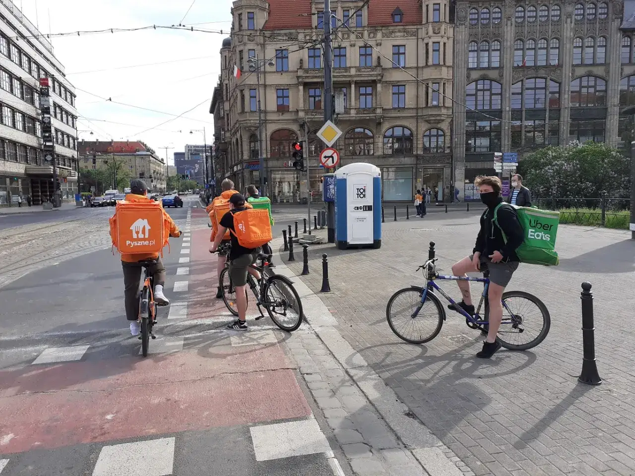 Kurierzy rowerowi z torbami Pyszne.pl i Uber Eats czekają na zielone światło. To obrazek z życia miasta 15 minutowego, gdzie wszystko jest blisko.