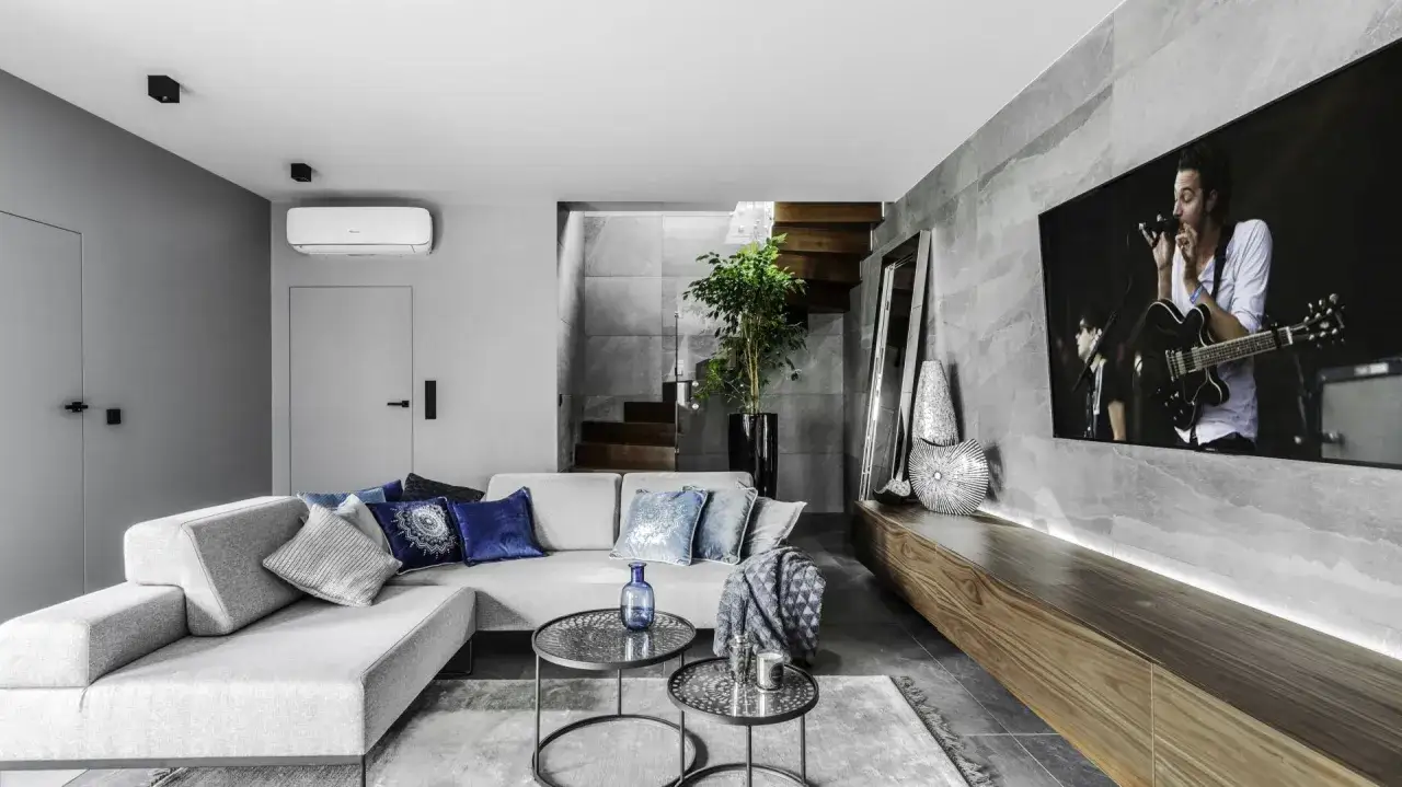 Nowoczesny salon z szarymi ścianami, kt&oacute;re świetnie komponują się z drewnianymi elementami i niebieskimi dodatkami.