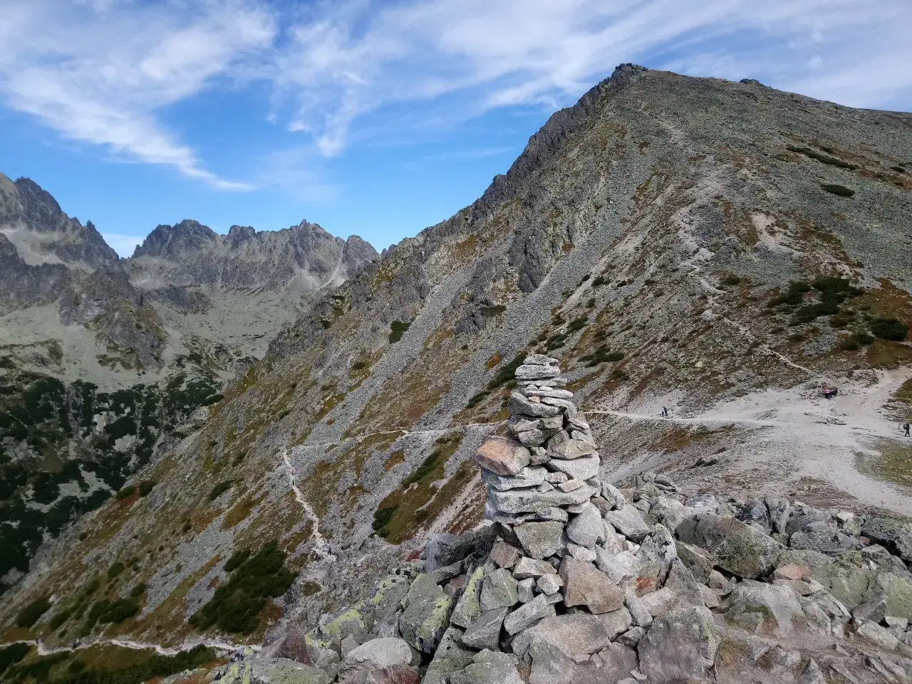 Kamienny kopiec na szlaku prowadzącym przez przełęcz pod Osterwą. W tle skaliste szczyty i błękitne niebo z chmurami.