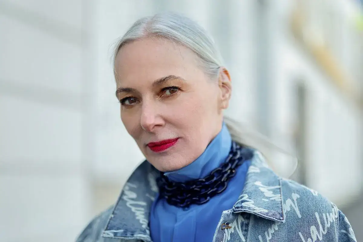 Elegancka kobieta z siwymi włosami, w niebieskiej koszuli i dżinsowej kurtce, pokazuje, jak nosić siwe włosy z klasą.