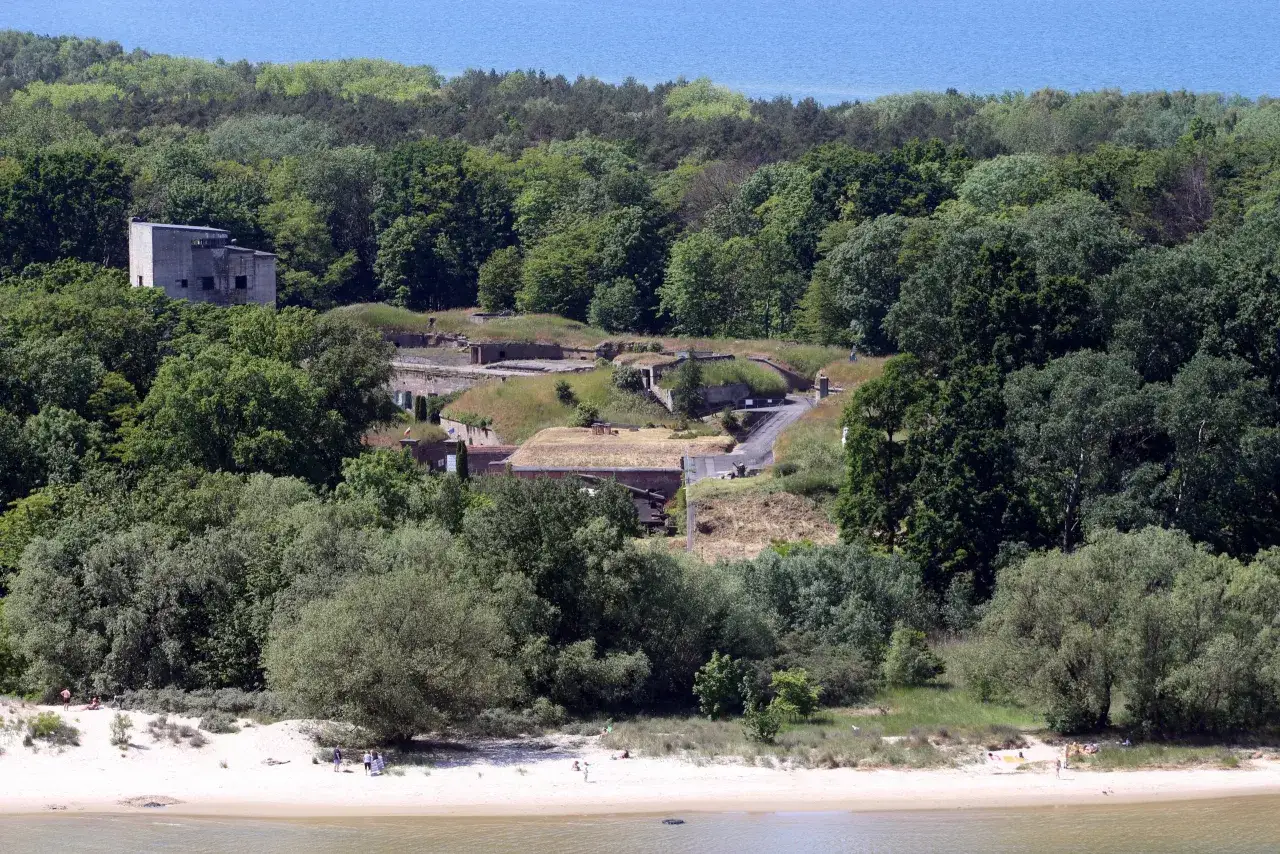 Plaża Cztery Wiatry z widokiem na fortyfikacje w lesie i błękitne morze.