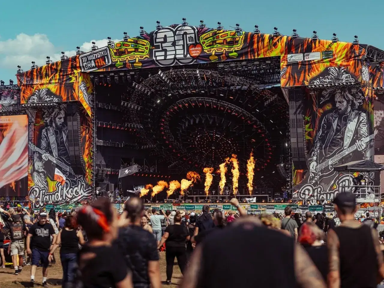 Wielka scena festiwalowa z płomieniami i wizerunkiem gitarzysty. Tu wszystko gra! Woodstock, gdzie jest?