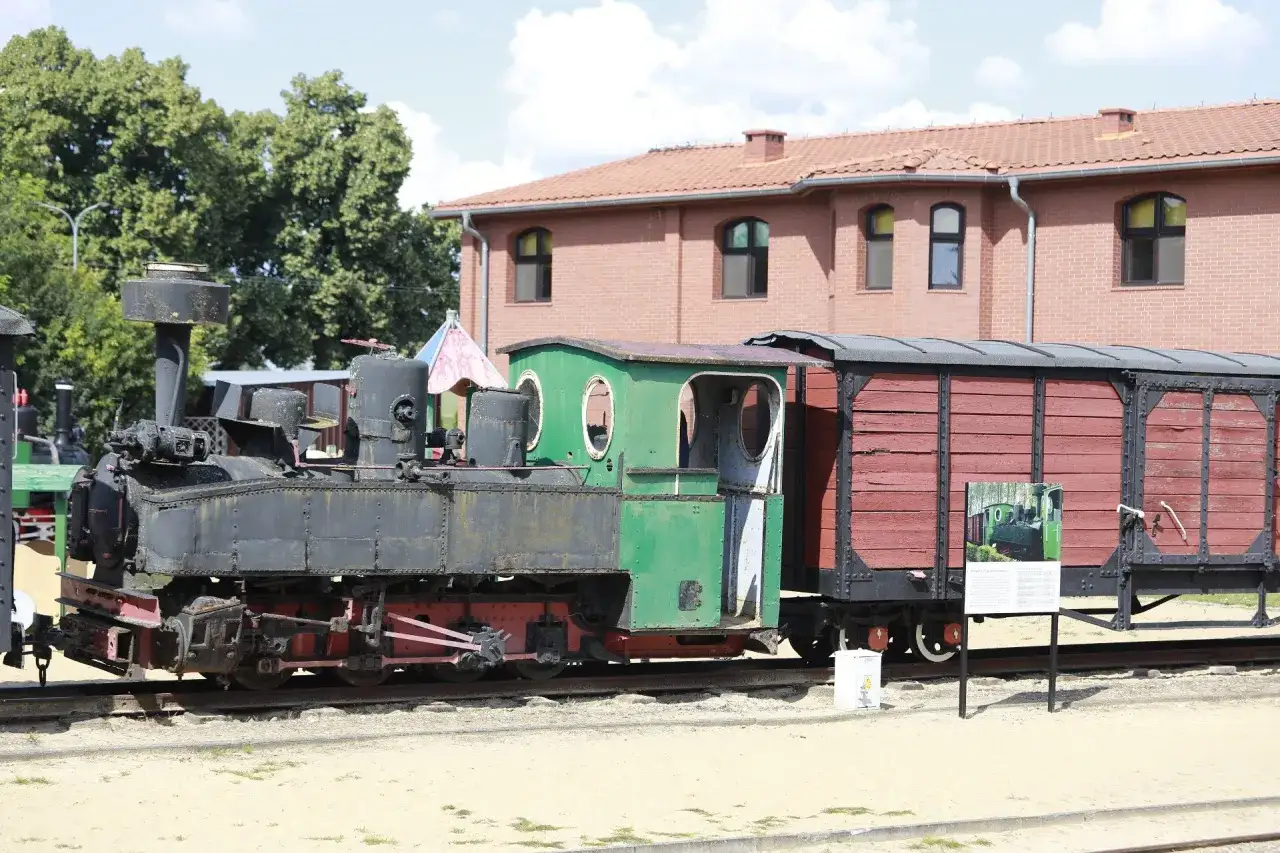 Czarna lokomotywa z zieloną kabiną i czerwoną skrzynią towarową na torach. To część zabytkowego szlaku kolejki wąskotorowej.