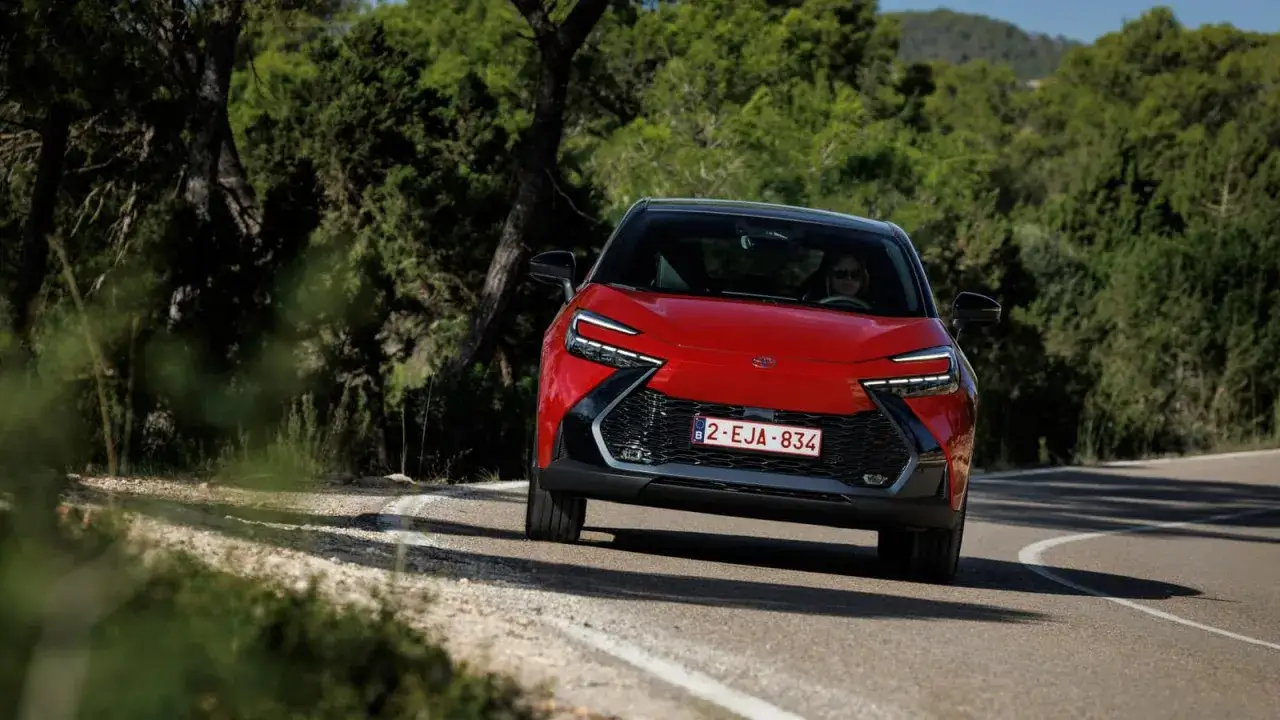 Czerwona Toyota C-HR na krętej drodze wśr&oacute;d zieleni. Zastanawiasz się, ile kosztuje nowa Toyota C-HR?