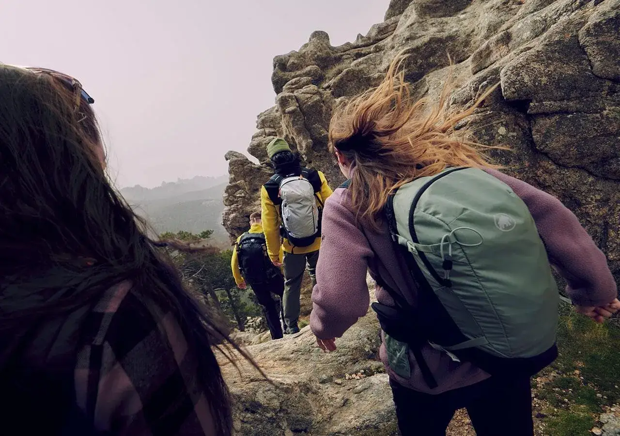 Grupa turystów w odzieży w góry wspina się po skalistym szlaku. Wiatr rozwiewa włosy jednej z osób.