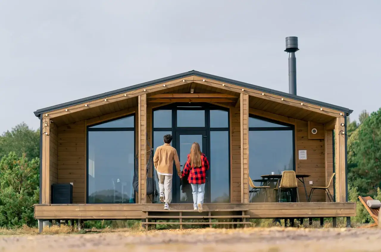 Para wchodzi do nowoczesnego domku letniskowego bez pozwolenia. Drewniana konstrukcja z dużymi oknami i kominem.