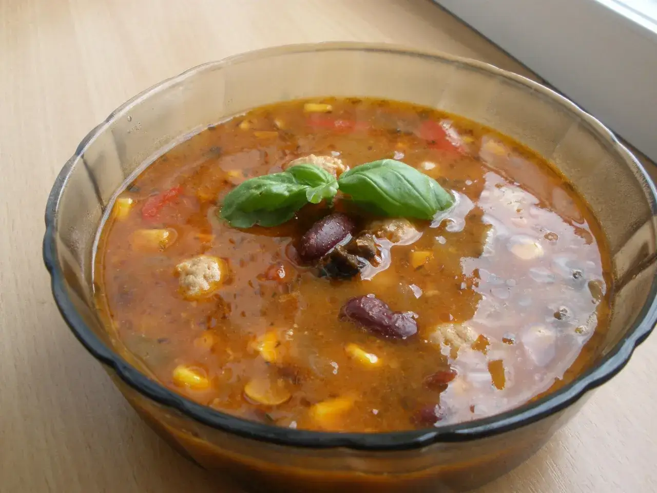 Aksamitna zupa meksykańska z pulpecikami, fasolą i kukurydzą, ozdobiona listkiem bazylii.