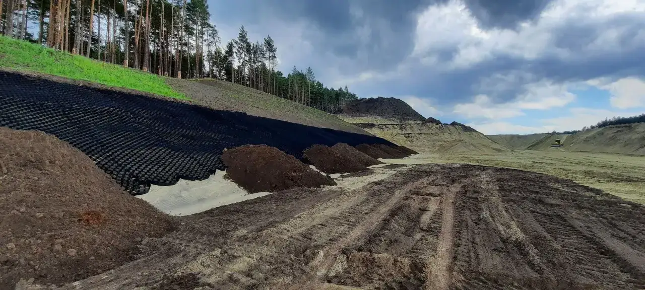 Montaż geokraty na skarpy w lesie. Teren budowy z maszynami i nasypami ziemi.