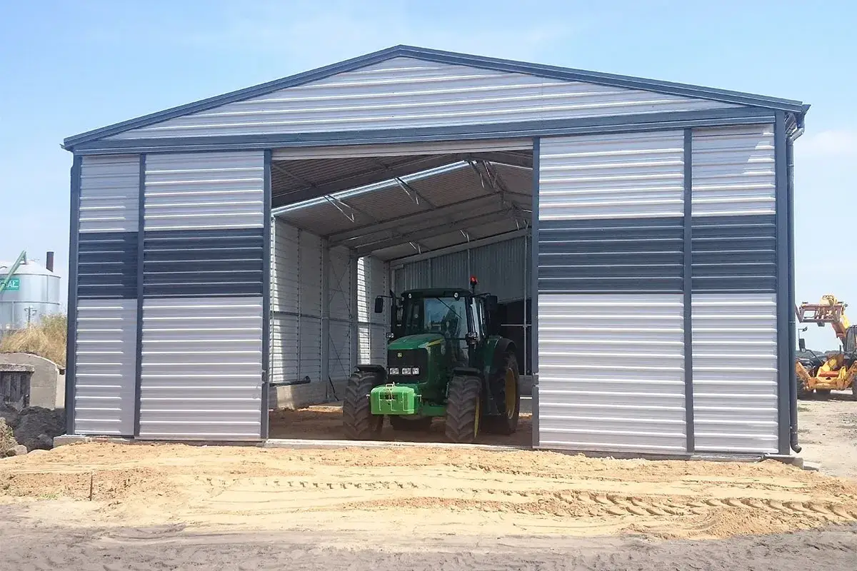 Nowy budynek gospodarczy z wiatą, w kt&oacute;rej stoi zielony traktor.