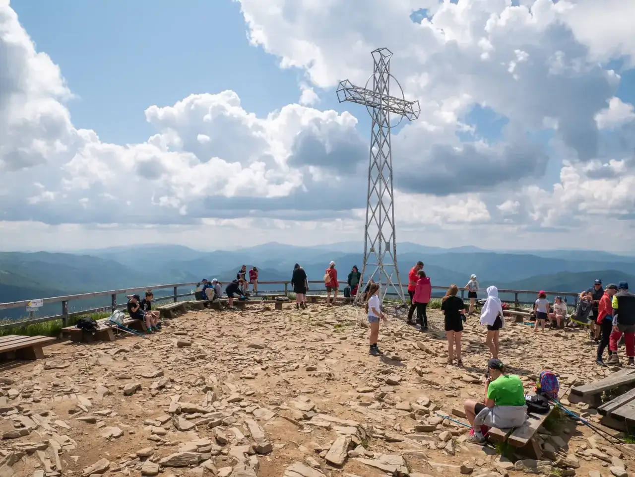 Ludzie odpoczywają na szczycie z krzyżem, podziwiając widok. Czy szlaki w Bieszczadach są otwarte? Tak, wygląda na to, że tak!