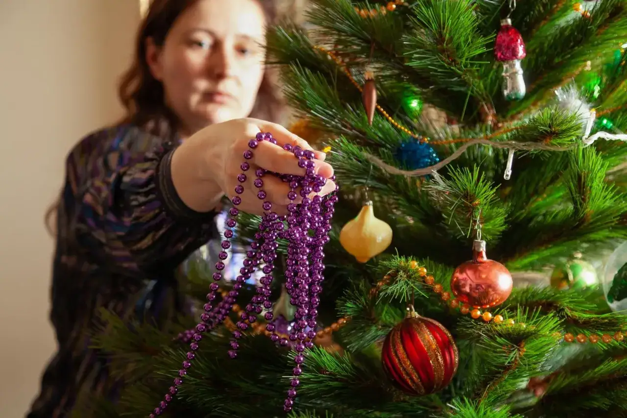Kiedy się ściąga ozdoby świąteczne, kobieta trzyma fioletowy sznur koralików przy choince.