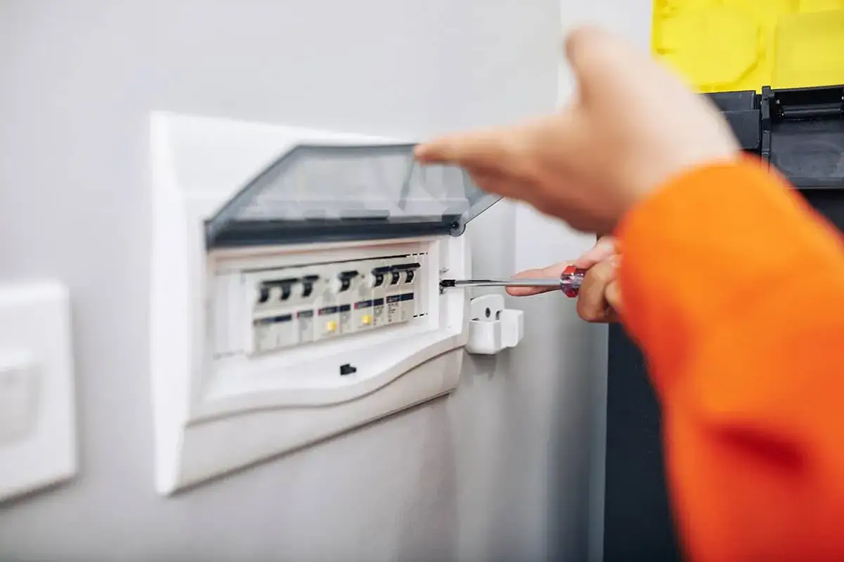 Ręka z wkrętakiem przy skrzynce z bezpiecznikami, przygotowanie do złożenia wniosku o przyłącze prądu.