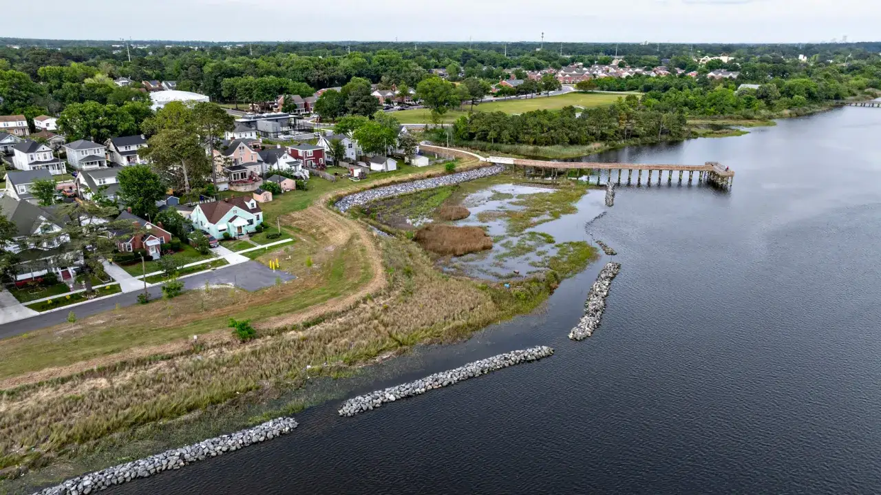 Fotografia z drona ukazuje nadbrzeżną dzielnicę z domami, falochronami i drewnianym molo.