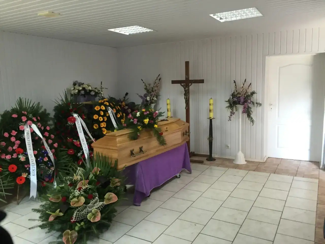 Drewniana trumna, krzyż i wieńce pogrzebowe tworzą scenę obrzędów pogrzebu.