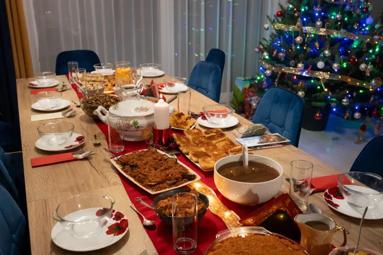 Stół wigilijny z potrawami, choinka w tle. Ile sztuk mięsa na osobę na imprezę? Trudno ocenić, ale wygląda na obficie zastawiony.