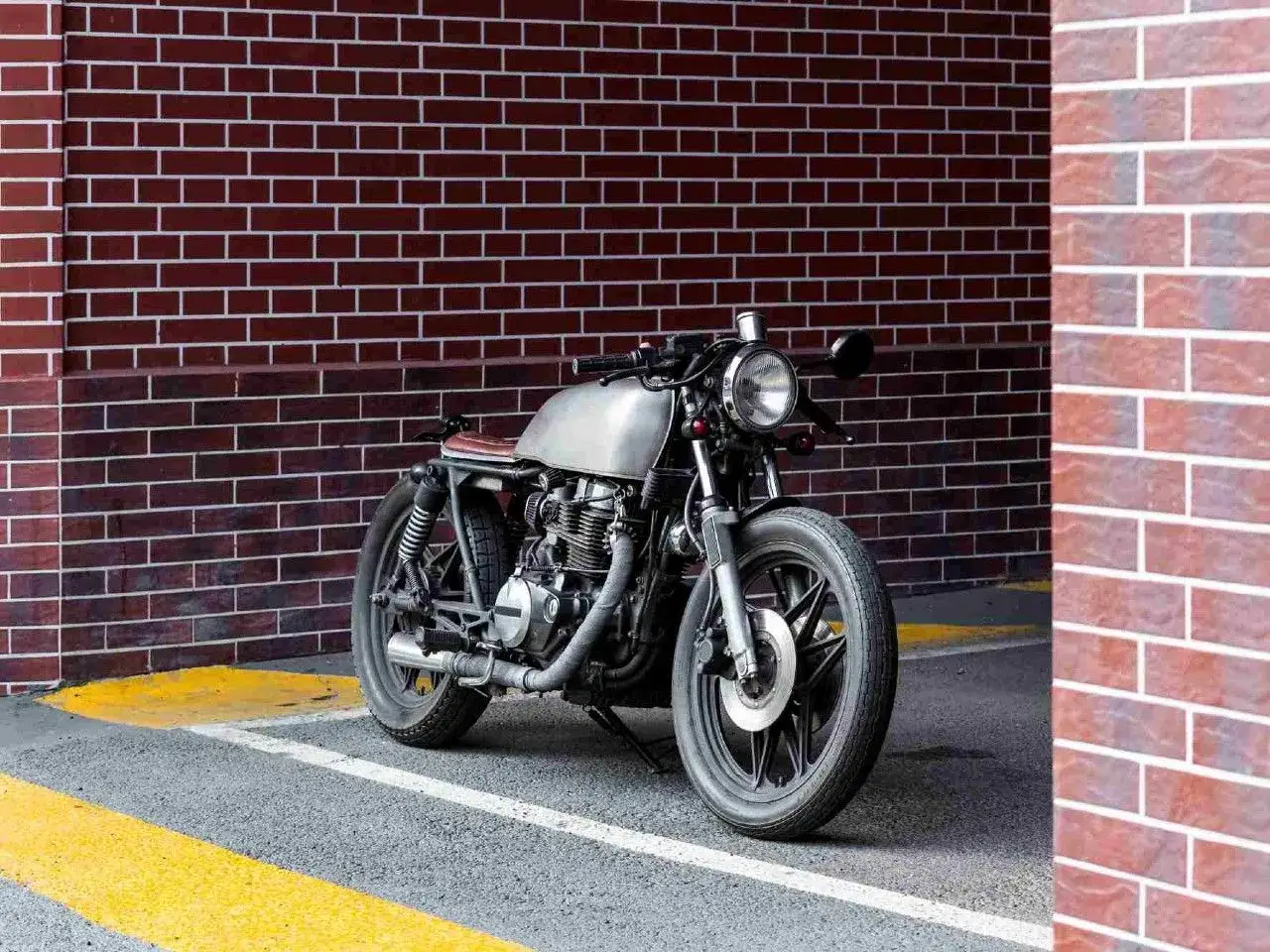 Stylowy motocykl miejski z metalicznym bakiem i brązowym siedzeniem stoi przy ceglanej ścianie.