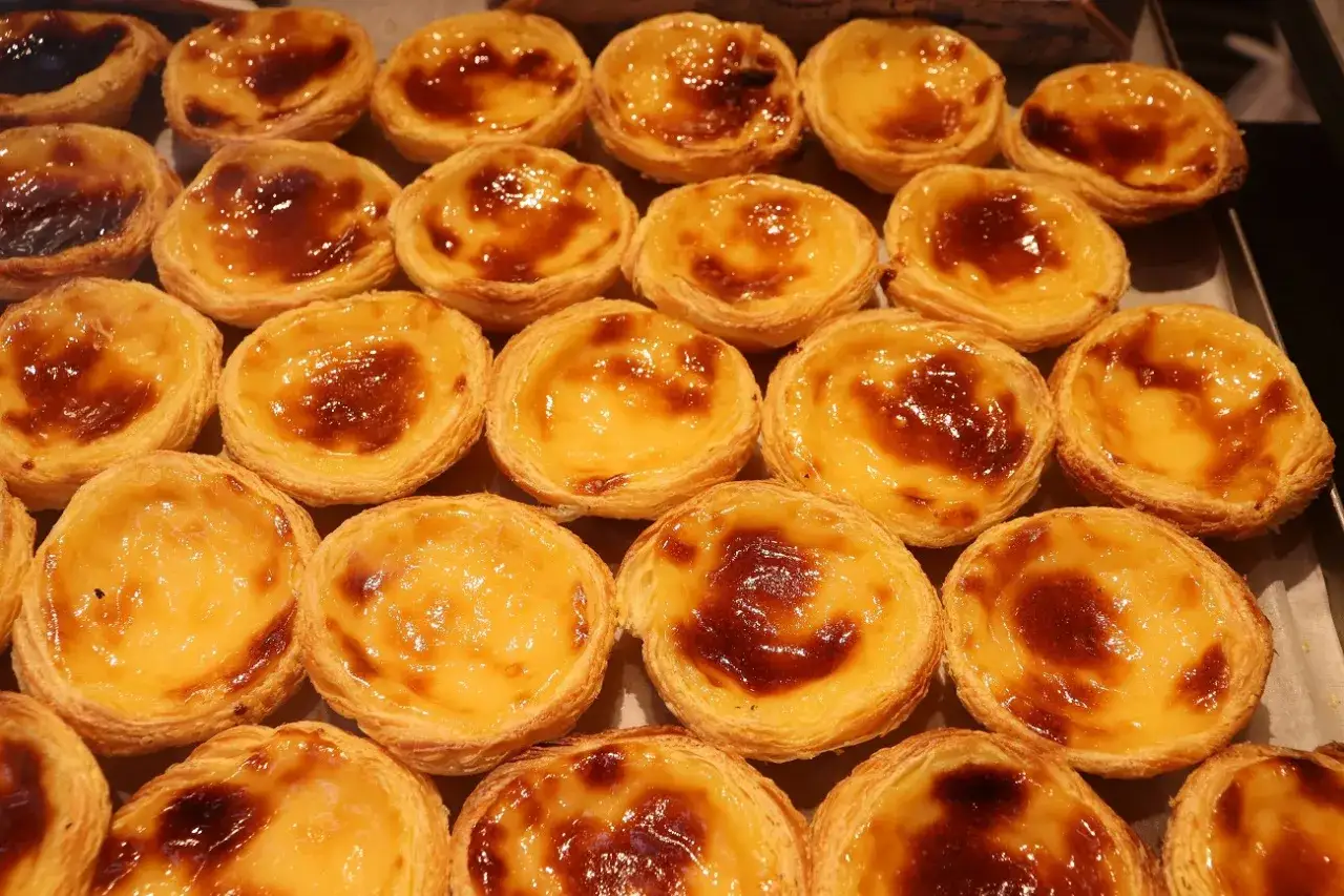 Mnóstwo pysznych, lekko przypieczonych babeczek portugalskich ułożonych na tacy.