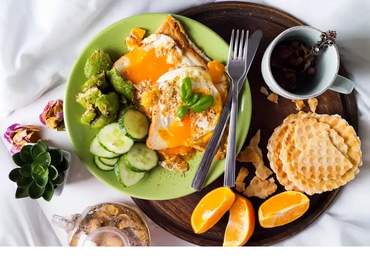 Pyszne wegetariańskie śniadanie: jajka sadzone na grzance, awokado, og&oacute;rek, pomarańcze i herbatka. Idealne pytanie: co zjeść na śniadanie wegetariańskie?