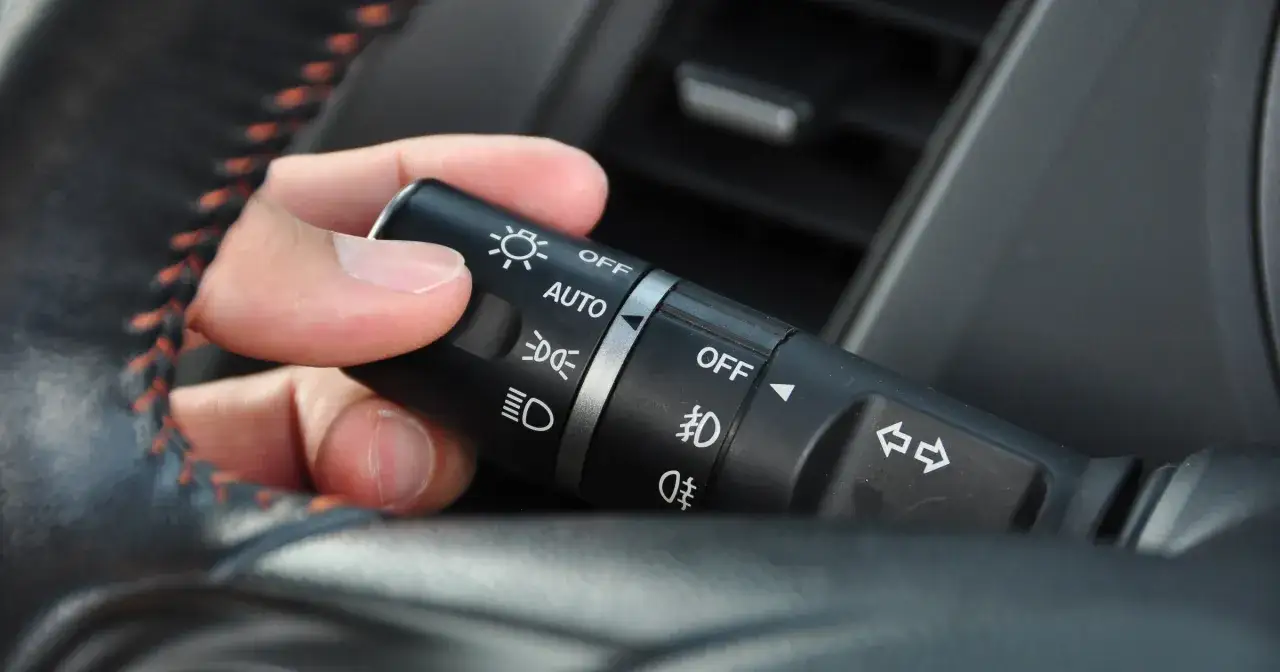 Dłoń ustawia przełącznik świateł na pozycję AUTO, pokazując, jak włączyć światła do jazdy dziennej.