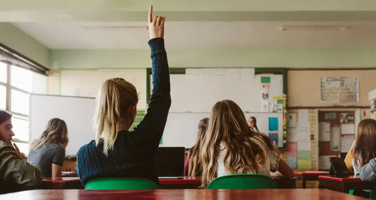 Uczennica z podniesioną ręką, jakby zadawała pytanie retoryczne po angielsku.