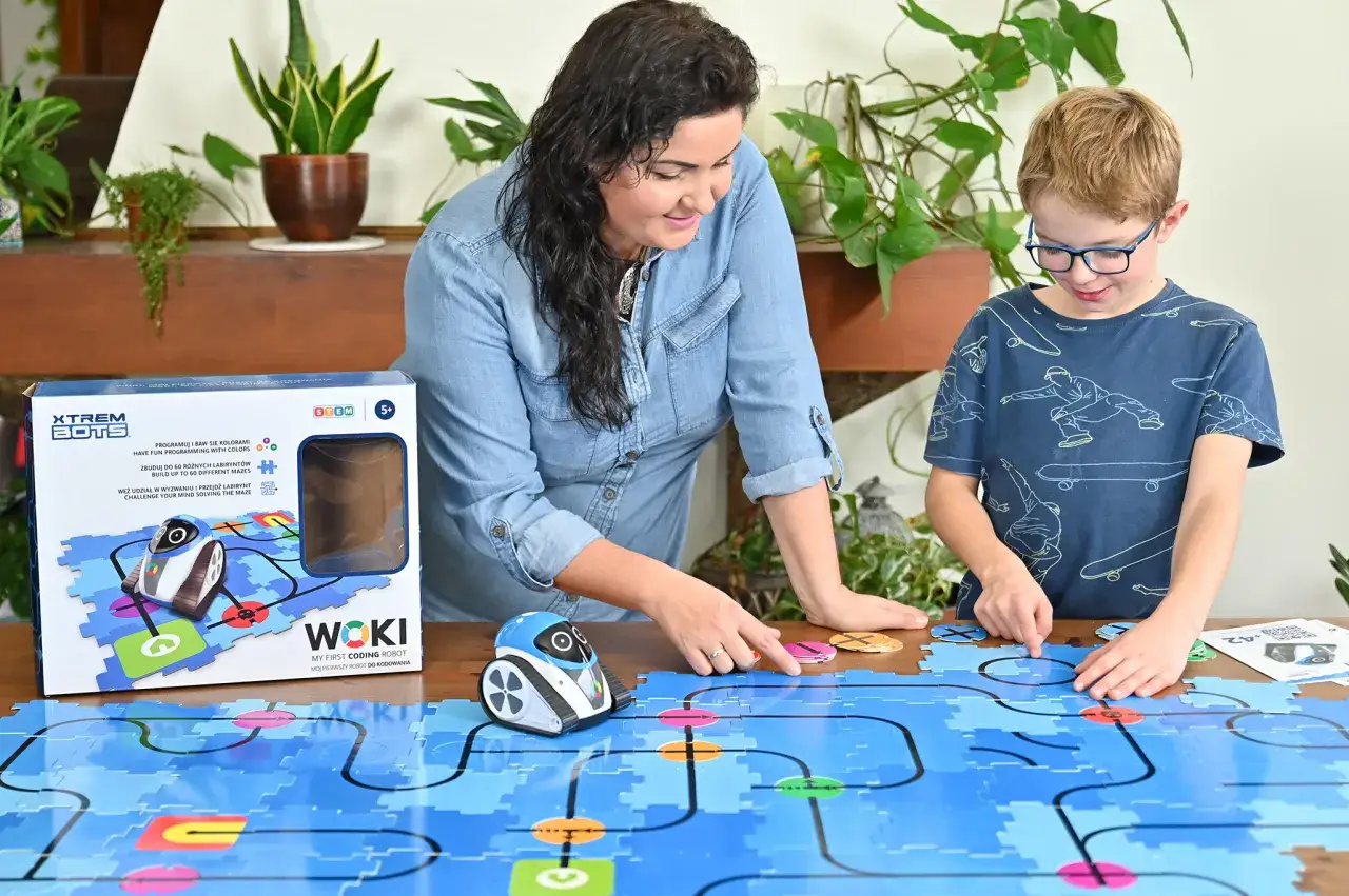 Mama i syn bawią się robotem WOKI, ucząc się kodowania dla 6 latka. Kolorowa mata i karty z zadaniami zachęcają do zabawy.