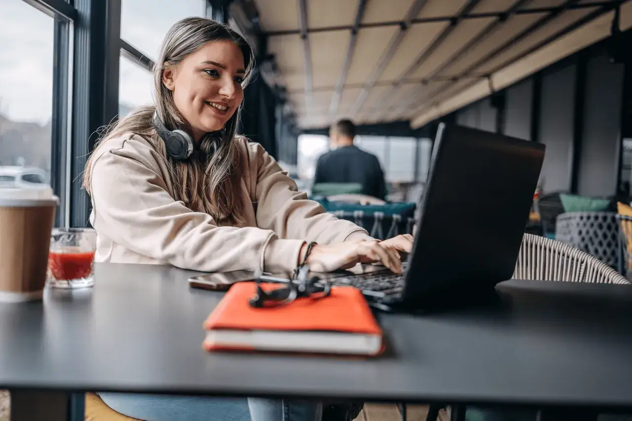 Uśmiechnięta dziewczyna z słuchawkami na szyi pracuje na laptopie. Zastanawia się, czy po zawodówce można iść do liceum, szukając odpowiedzi w internecie.