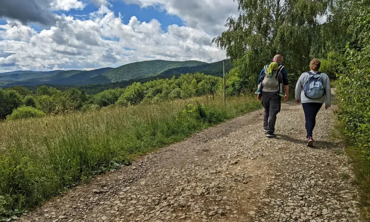 Rodzina wędruje szlakiem w kierunku bac&oacute;wki pod Małą Rawką. G&oacute;ry i lasy w tle.