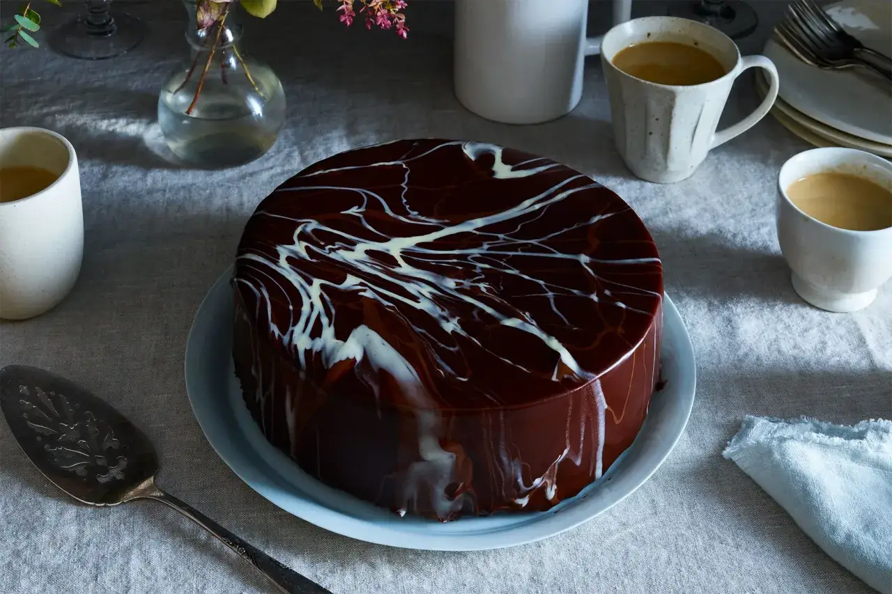 Elegancki tort oblany błyszczącą, prostą polewą czekoladową z czekolady, ozdobiony białymi smugami.