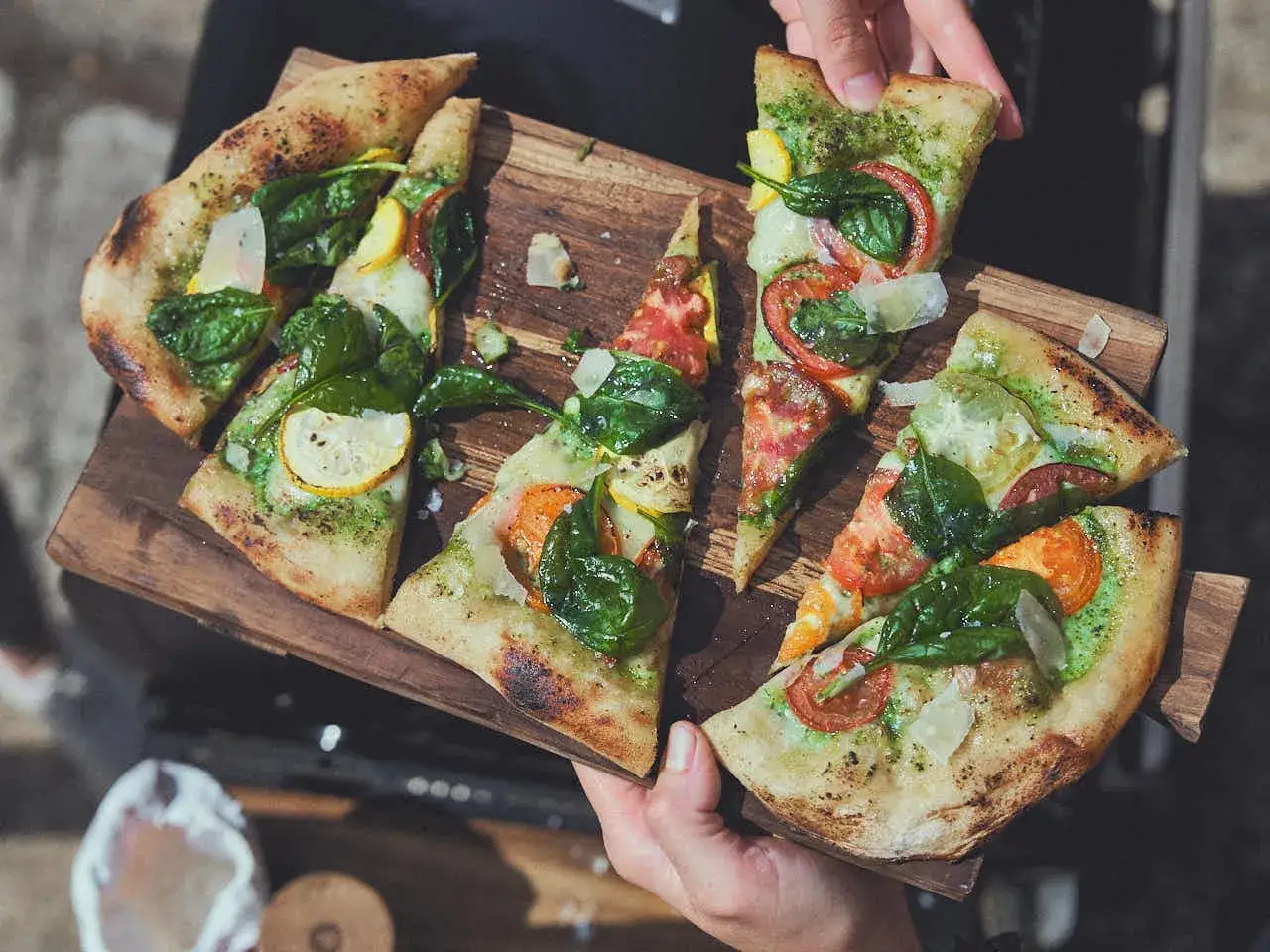 Pyszna pizza z zielonym pesto, pomidorami, szpinakiem i plasterkami cukinii, podana na drewnianej desce.