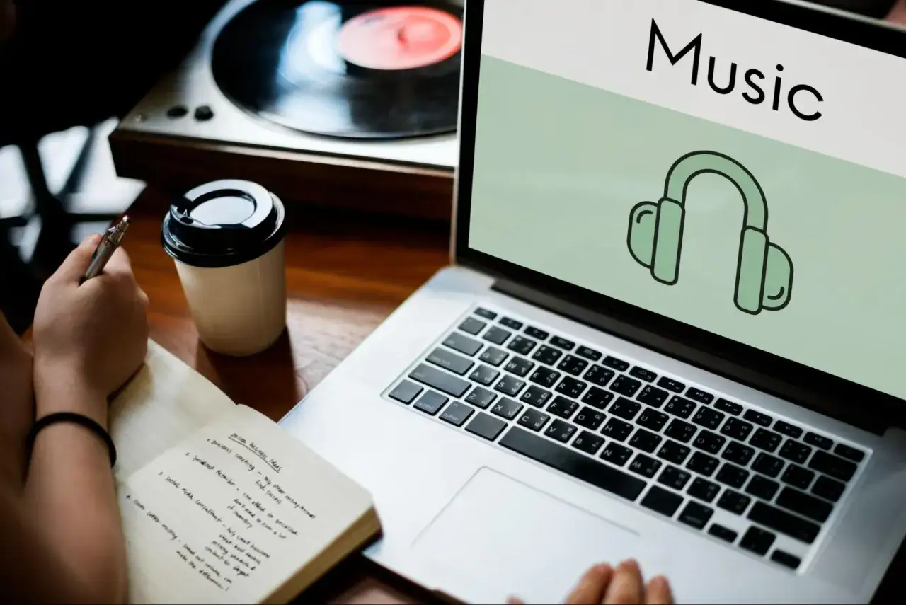 Osoba notuje pomysły na biznes, słuchając muzyki z laptopa, który pokazuje jak pobrać muzykę na komputer.
