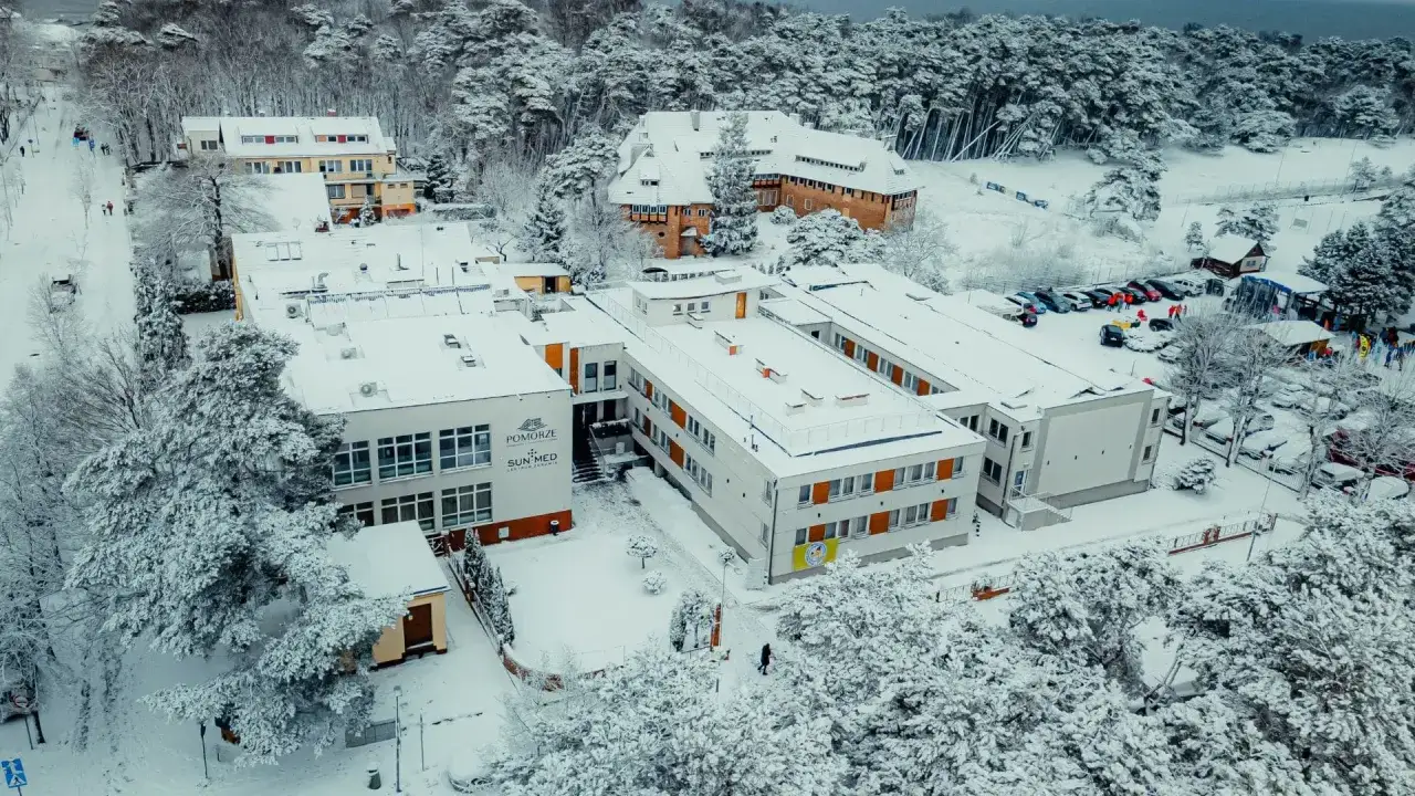 Zimowy turnus rehabilitacyjny nad morzem z dofinansowaniem PFRON. Ośnieżone budynki centrum rehabilitacyjnego i las.